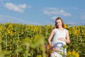 A pregnant girl in dress is standing with a yellow sunflower in the field. Pregnant woman holding her belly against the background Royalty Free Stock Photo