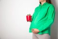 A pregnant girl in a green blouse holds a red cactus pot. Coznept of cutting pains and colic in the abdomen in pregnant