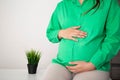 A pregnant girl in a green blouse holds on to her stomach, which has pain and bloating in her stomach. Discomfort and