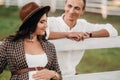 A pregnant girl in a hat and her husband in white clothes stand next to the horse corral.a stylish couple waiting for a child Royalty Free Stock Photo