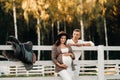 A pregnant girl in a hat and her husband in white clothes stand next to the horse corral.a stylish couple waiting for a child Royalty Free Stock Photo