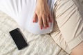 A pregnant girl holds a mobile phone near her belly. The concept of harm and deviations in the development of the unborn