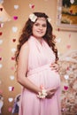 Pregnant girl with long red hair in a long pink dress in a classic interior. waiting for a baby