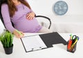 a pregnant girl in the office at work signs documents. The concept of pregnancy and going on parental leave. Rights and Royalty Free Stock Photo