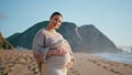 Pregnant girl posing seashore with happy smile. Expectant mother standing beach. Royalty Free Stock Photo