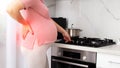 Pregnant girl prepares food in the kitchen. The concept of heaviness and discomfort in the last trimester of pregnancy