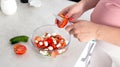 A pregnant girl prepares a vegetable salad of cucumbers and tomatoes. The concept of nutrition of pregnant women with vitamins and