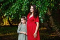 A pregnant girl in a red dress with her daughter next to green leaves. Portrait of a beautiful family of a pregnant woman in natur Royalty Free Stock Photo
