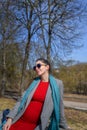 Pregnant girl in a red dress in the park. Portrait of a beautiful pregnant woman in a red dress and blue scarf, in a gray coat Royalty Free Stock Photo