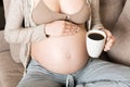 Pregnant girl sitting on sofa with coffee Cup in hand coffee. maternity morning