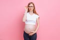 Pregnant girl in a t-shirt with glasses for the visually impaired. on pink background