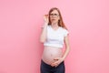 Pregnant girl in a t-shirt with glasses for the visually impaired. on pink background