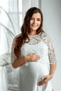 A pregnant girl in white clothes stands on a light background. Beautiful belly of a young attractive pregnant girl. Family, Royalty Free Stock Photo