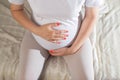 A pregnant girl in white holds her hands on her stomach, she has bloating and flatulence. Gas formation in the