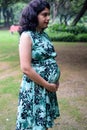 A pregnant Indian lady poses for outdoor pregnancy shoot and hands on belly, Indian pregnant woman puts her hand on her stomach