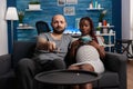 Pregnant interracial couple looking at camera watching television Royalty Free Stock Photo