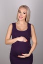 Pregnant lady in a dress hugging her tummy. Close up. Gray background Royalty Free Stock Photo