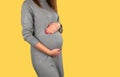 Pregnant lady. In a gray suit. Standing. She`s holding her belly, which is pregnant with her hands, from the bottom and top.