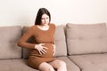 Pregnant Lady Having Massaging Lower belly Sitting On Sofa Indoor. Pregnancy Problems Concept. Maternity healthcare Royalty Free Stock Photo