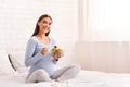 Pregnant lady holding bowl with salad sitting in bed indoor Royalty Free Stock Photo