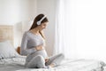 Pregnant lady seated on bed caressing her belly