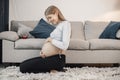 Pregnant lady sitting near a sofa in living room and touching her belly Royalty Free Stock Photo