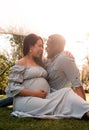 Pregnant Latina woman and African man couple sitting in a lush green bright sunlit park