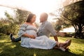 Pregnant Latina woman and African man couple sitting in a lush green bright sunlit park