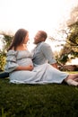 Pregnant Latina woman and African man couple sitting in a lush green bright sunlit park