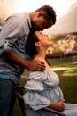 Pregnant Latina woman in a dress sitting on a chair while her African husband kissing her forehead