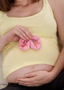 Pregnant with a little princess. a young pregnant woman holding a pair of pink baby shoes against her belly. Royalty Free Stock Photo