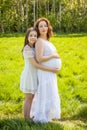 Pregnant mother with her daughter white dress in the green park sunny day