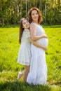 Pregnant mother with her daughter white dress in the green park sunny day