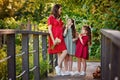 A pregnant mother in a red dress and her two daughters in nature. The family is standing on the bridge holding a bouquet of Royalty Free Stock Photo