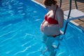 Pregnant red-haired woman in the pool in a red bikini. Royalty Free Stock Photo