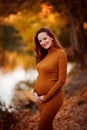 Pregnant in slinky dress in autumn Park by river. Royalty Free Stock Photo