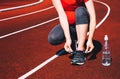 Pregnant sporty woman lacing sneakers on sport stadium.