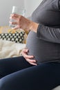 Pregnant, thirsty, woman drinking water from a glass while sitting comfortably on the sofa Royalty Free Stock Photo