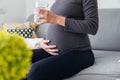 Pregnant, thirsty, woman drinking water from a glass while sitting comfortably on the sofa Royalty Free Stock Photo