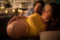 Pregnant wife is lying on bed in bedroom and in background you can see curious husband. Woman in advanced pregnancy.