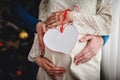 A pregnant wife, man holds her arms around the round stomach. Holds a decorated heart with a ribbon. View of the stomach pregnant Royalty Free Stock Photo