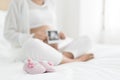Pregnant woman with baby shoes on bed at home. Enjoying her spec Royalty Free Stock Photo