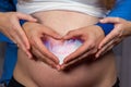 The shore of a pregnant woman - the hands of a dad and a mother in the form of a heart on the stomach with a picture of the child Royalty Free Stock Photo