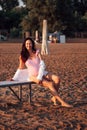 pregnant woman on the beach, smiling pregnant woman in a pink swimsuit sitting on a bench on a sandy beach in summer at Royalty Free Stock Photo