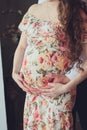 Pregnant woman in a beautiful colorful dress and her husband hugging the tummy