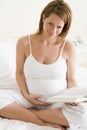 Pregnant woman in bedroom reading book smiling Royalty Free Stock Photo