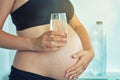 Pregnant woman belly holding a glass of water suggesting importance to hydrate during pregnancy