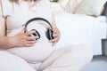 pregnant woman with big belly applying headphones to her belly for prenatal music stimulation