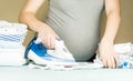 Pregnant woman with big belly preparing, ironing newborn baby clothes before labor Royalty Free Stock Photo