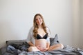 Pregnant woman in black lingerie holding her belly and sitting on bed. Royalty Free Stock Photo